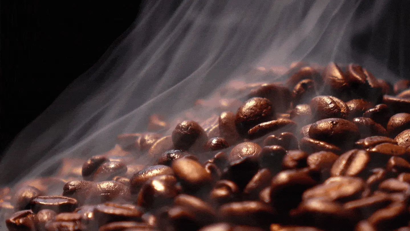 A close up of coffee beans with smoke coming from the top.